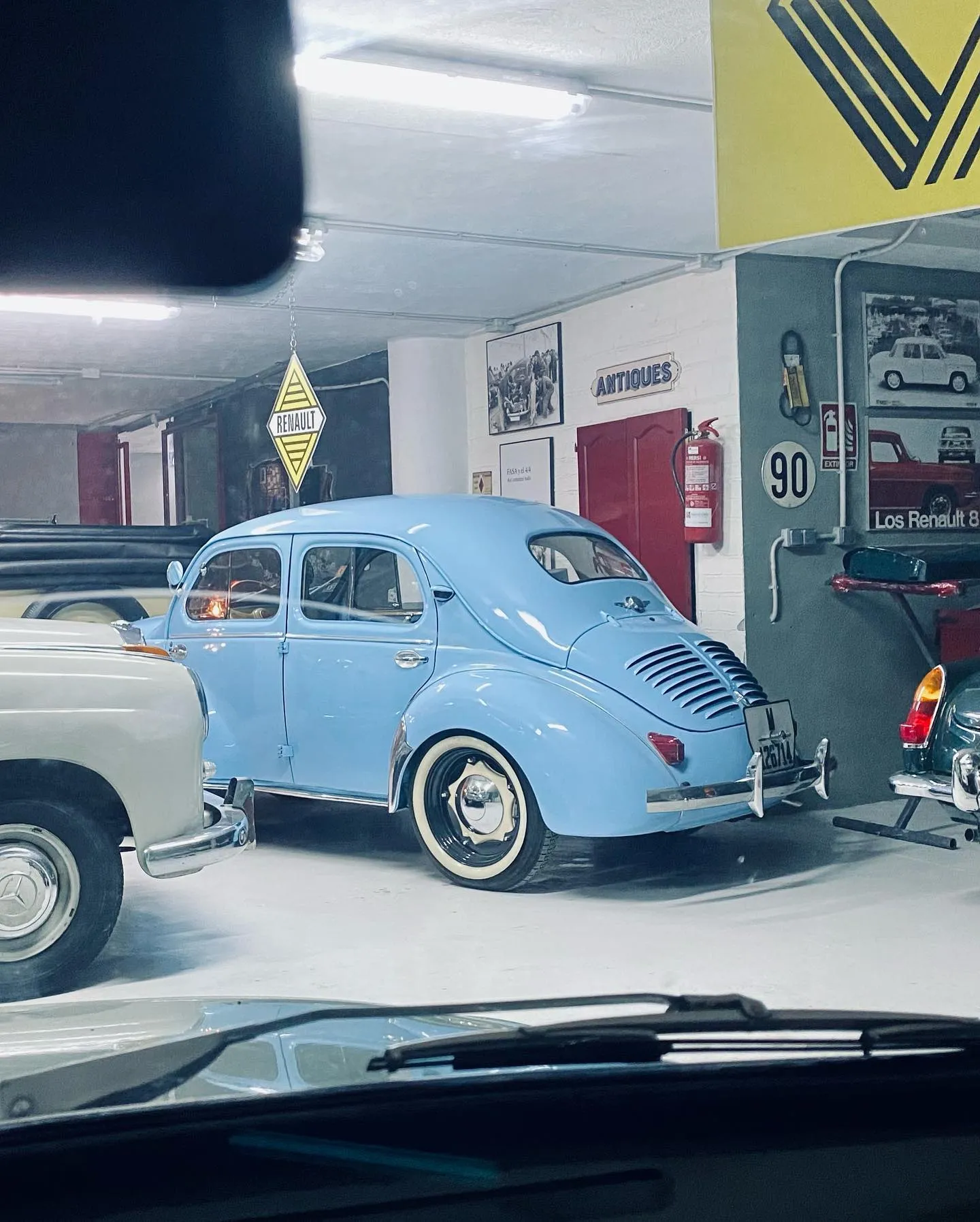 Interior del garaje con un Renault 4CV azul y carteles vintage