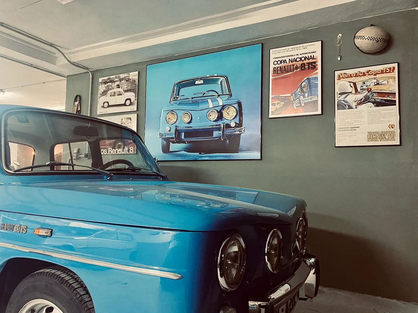 Un rincón del garaje de The Vint-Garage: un Renault 8 TS azul bajo los carteles de la Copa Nacional, visto como desde el asiento de un Renault 4