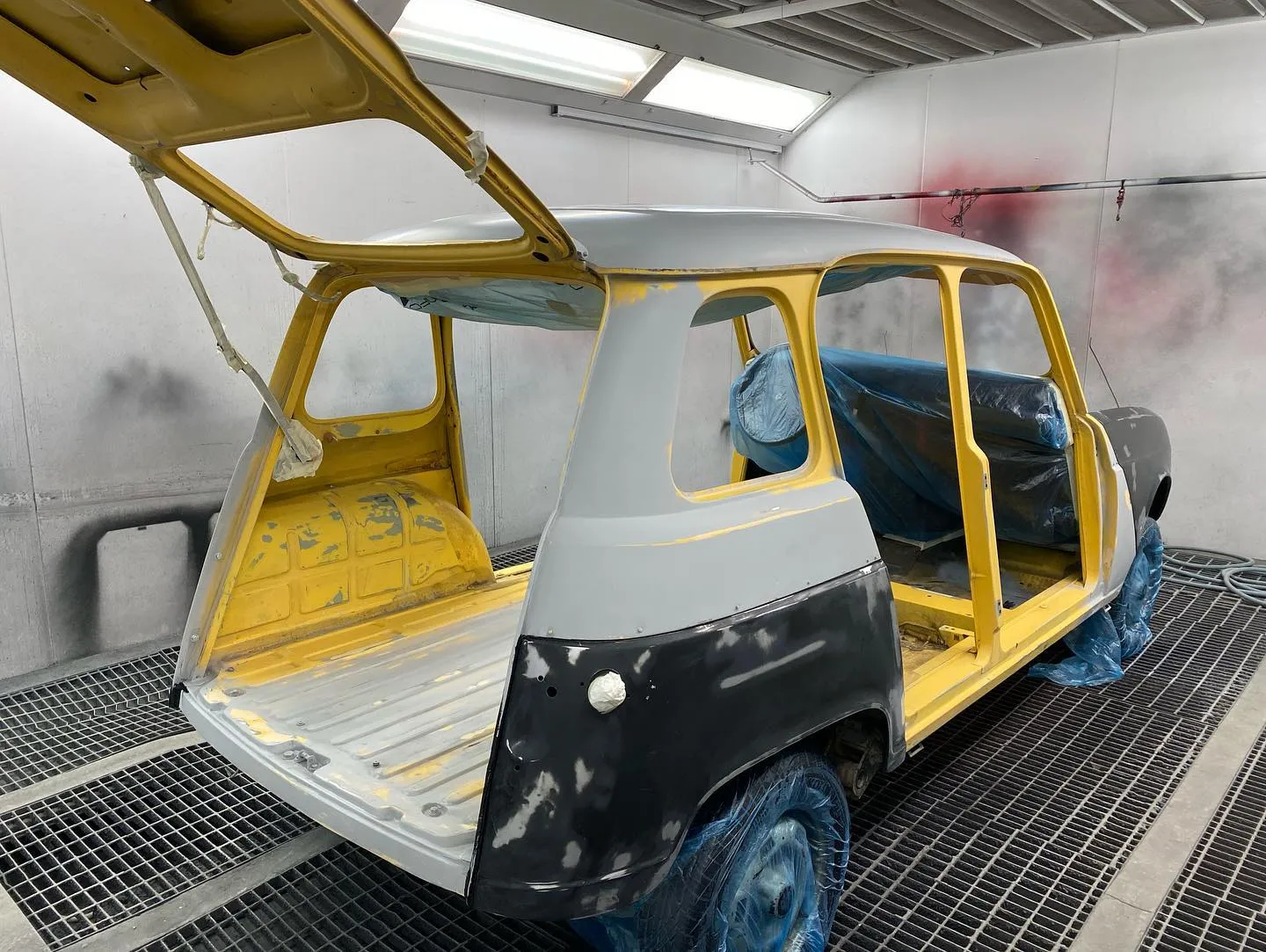 La carrocería del Renault 4 amarillo desmontada y en imprimación gris, con las masillas a la vista y las ruedas embolsadas